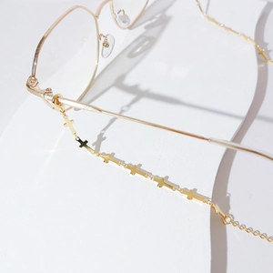 Gold plated eyewear chain featuring minimalist cross charms on white stone surface