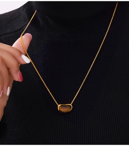 Détail d'un collier vintage en acier titane avec un pendentif haricot en oeil de tigre brun