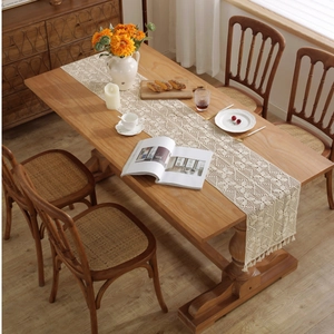 Handmade beige crochet table runner with lace patterns and tassels on a wooden dining table