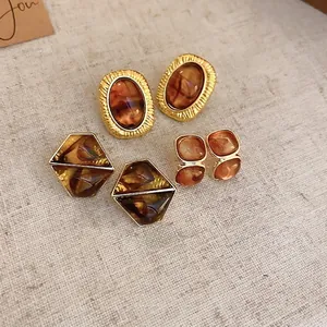 Three pairs of vintage gold-plated resin earrings with amber tones on beige linen