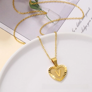 Macro detail of golden heart pendant with engraved letter V and textured finish