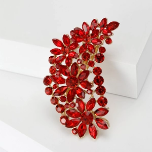 Detailed macro view of an oversized gold flower brooch with faceted red crystal gemstones