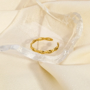 Close-up of gold woven hollow ring on clear acrylic props with beige silk background