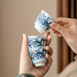 Ceramic tea cups with blue and white dragon pattern and gold trim in hand