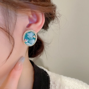 Close-up of vintage cameo earrings with blue silhouette and gold rim worn by model