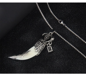 Detailed view of wolf tooth pendant with silver reaper carving on a box chain necklace