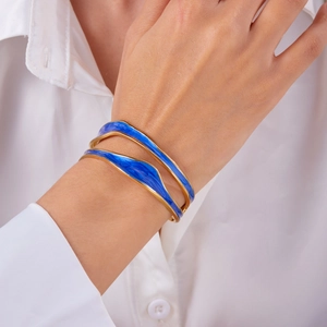 Close-up of wavy gold-plated bangle with deep blue enamel details on woman's wrist