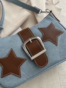 Detail of blue denim shoulder bag with brown leather star patches and large metal buckle