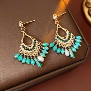 Detailed macro of golden teardrop tassel earrings with green crystals and pearls