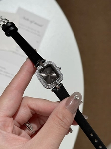 Close-up of square rhinestone-encrusted silver watch with black leather strap and Roman numerals