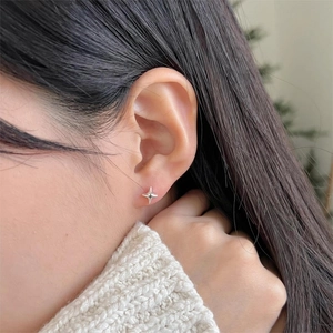 Close-up of a silver four-pointed star stud earring worn on a model's ear