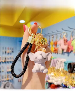 Detail of white elephant keychain with gold crown, bell and black leather strap