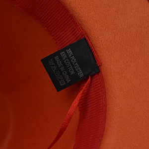 Detail view of the orange fedora hat's care label showing cotton and polyester fabric blend