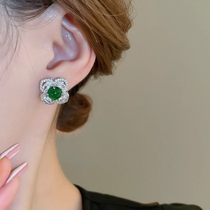Close-up of vintage flower stud earring featuring emerald green stone and silver diamonds