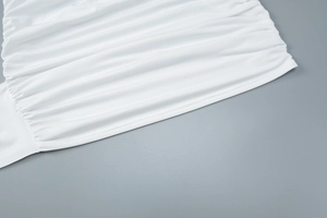Detailed close-up of white ruched fabric texture with elegant pleats on a mini dress