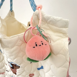 Nahaufnahme von Pfirsich-Plüsch-Anhänger mit Acrylkette an einer weißen gesteppten Tasche