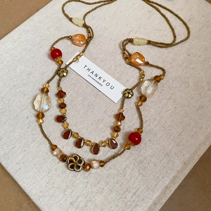 Détail d'un collier multicouche vintage avec gouttes d'ambre et accents de fleurs en céramique