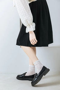 Detail of white lace mesh crew socks with ruffle cuffs paired with black platform loafers