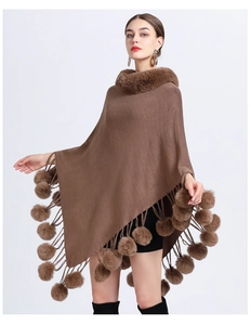 Detail of a brown knitted poncho featuring a plush faux fur collar and decorative pom poms