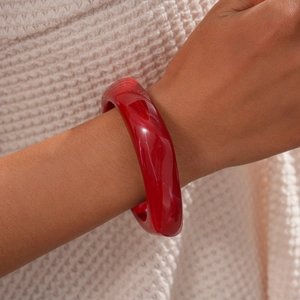Close-up of a chunky deep red resin bangle worn by a model against white knitwear