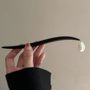 Detail of a black wooden hair stick featuring a delicate white baroque pearl pendant