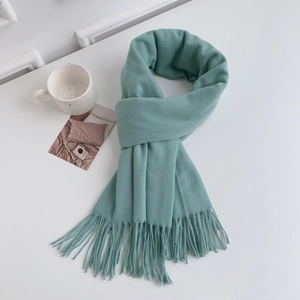 Flat lay of a soft green solid color scarf with fringes next to a ceramic cup