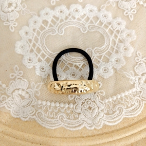 Close-up of golden hammered metal alloy ornament on a black elastic hair tie for women