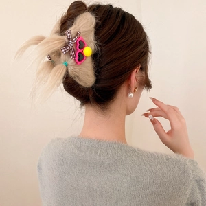 Detail view of a large beige plush hair claw clip with cherry and bow on a hairstyle