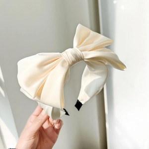 Detail of a beige silk bow headband featuring elegant fabric texture and minimalist style
