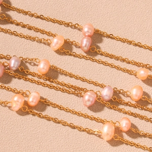 Elegant gold chain necklace with pink and lavender freshwater pearls on beige background