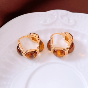 Macro shot of gold-framed amber resin hoop earrings on a decorative ceramic tray