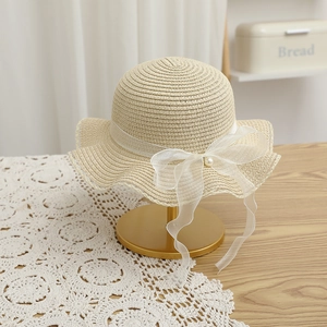 Detail of beige straw hat featuring a translucent chiffon bow and decorative pearl accent