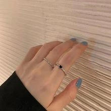 Close-up of stacked silver rings featuring a chain link band and a black heart charm