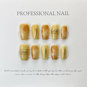 Detail of luxury yellow amber press-on nails with gold foil and metal chain accents