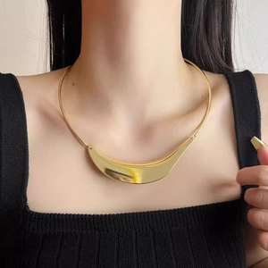 Macro shot of minimalist gold crescent-shaped metal collar necklace on a black sweater