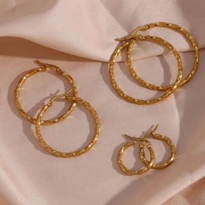 Three sizes of gold twisted hoop earrings set on champagne silk background texture