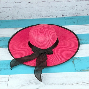Detail of rose pink wide brim straw hat with black ribbon bow and textured weave