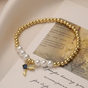 Detailed close-up of pearl bracelet with golden bird charm and blue teardrop gemstone
