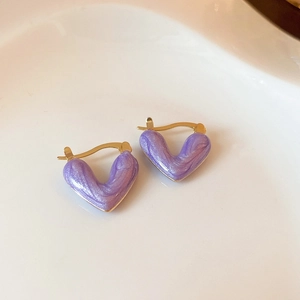 Macro shot of heart-shaped purple tiger eye earrings with golden metal edges on white tray