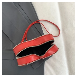 Detail of red heart-shaped crossbody bag featuring silver metal zippers and smooth texture