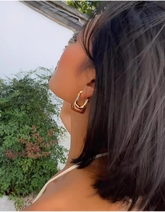Close-up of a U-shaped gold resin earring worn by a model in soft outdoor lighting