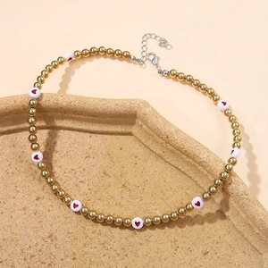 Detail of gold beaded necklace featuring white beads with red hearts on a beige tray