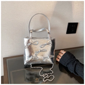 Detail of silver metallic handbag with decorative bows and beaded chain strap