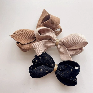 Three gold polka dot corduroy bow hair clips in tan, beige, and black on white background