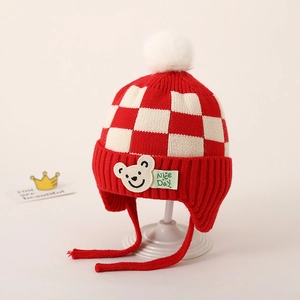 Detail van rood-wit geruite gebreide babymuts met beerpatch en witte pluche pompon