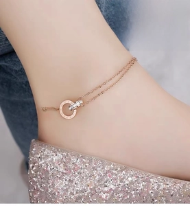 Close-up of double-layer rose gold anklet with interlocking Roman numeral and crystal rings