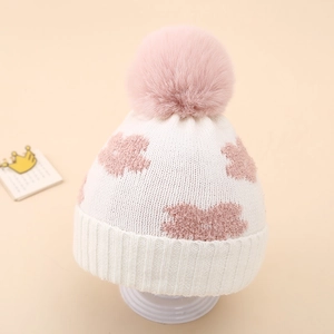 Macro detail of infant knit beanie featuring pink floral patterns and plush pom-pom
