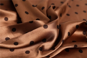 Close-up detail of smooth satin fabric with brown base and black polka dot pattern