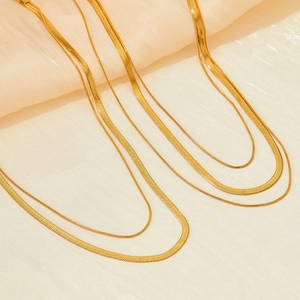 Three-layer gold snake chain stainless steel necklace displayed on soft beige fabric