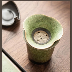 Close-up of a petal-shaped green ceramic tea strainer with a fine metal mesh filter
